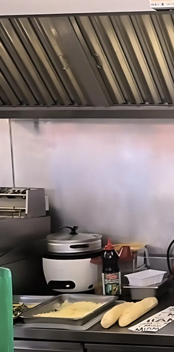 La cuisine ouverte en inox : hotte, bac de fromage râpé et pains prêts à garnir